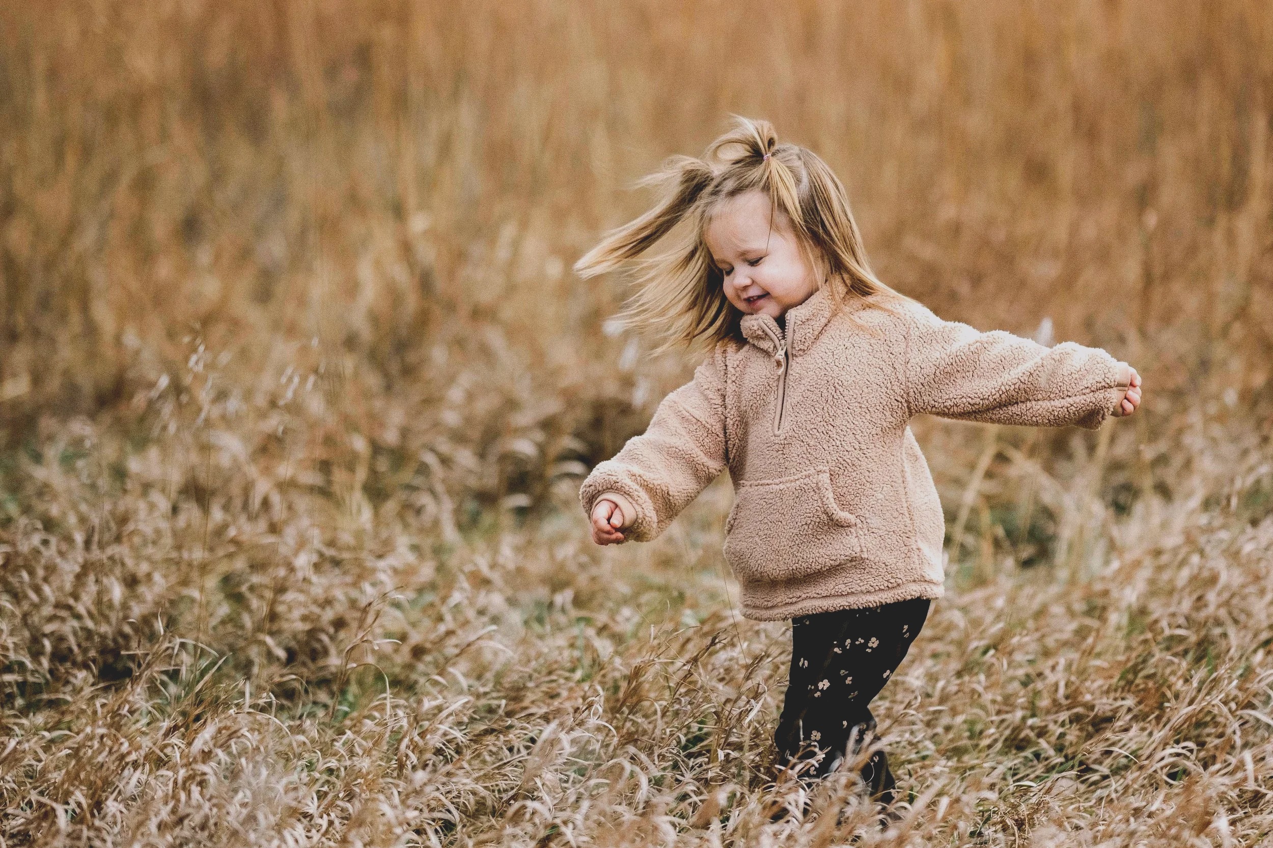 A little girl running through tall prairie grass in the late afternoon